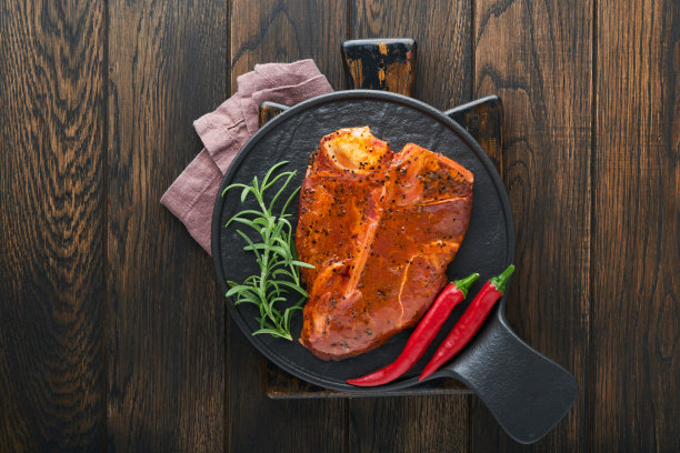 生牛排、t骨或上肉排。t骨牛排或上肉排配调味料、盐和迷迭香，放在混凝土背景的黑色陶瓷盘上。前视图。文本。图片下载