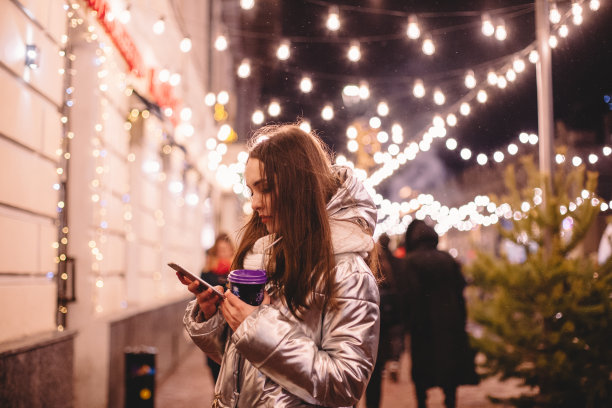 圣诞节期间，年轻女子站在城市街道上使用智能手机图片下载