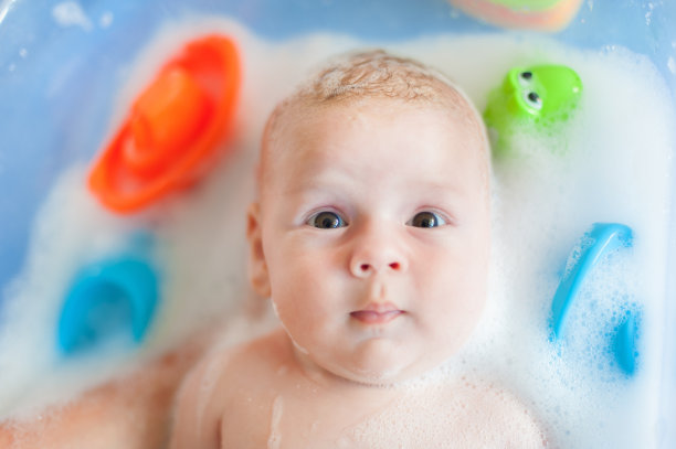 母亲在浴缸里给婴儿洗澡，浴缸里有水，肥皂泡冒出来图片下载