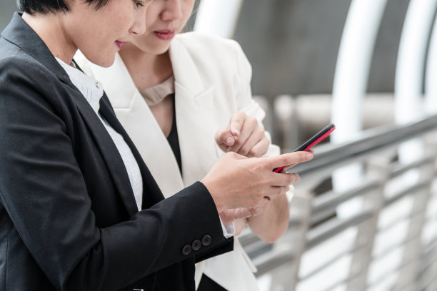 两名亚洲妇女正在使用数字平板智能手机与商业伙伴在街道城市的办公室外会面。团队合作女性在户外办公室讨论团队合作的建议。图片下载