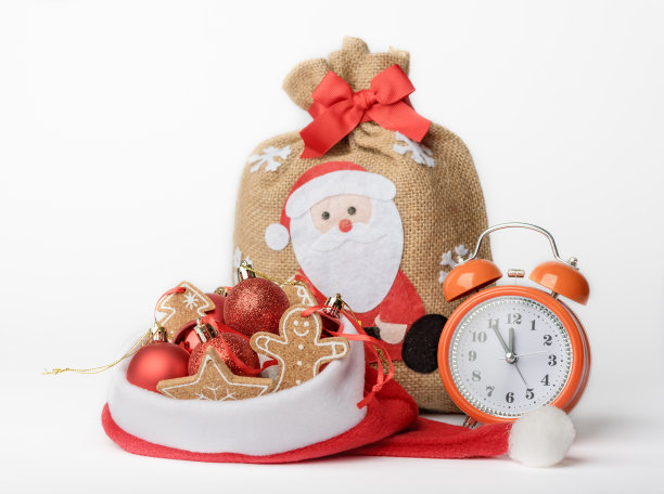 新年前夜的概念照片，一个闹钟，一个装着礼物的袋子和圣诞老人帽子上的圣诞树装饰图片下载