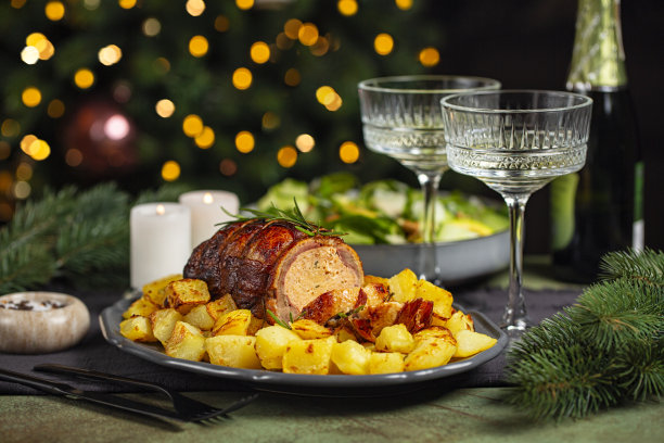 圣诞节或新年的餐桌。特写的烤鸭卷塞满肉和橙子，烤土豆，沙拉，香槟杯在圣诞树前和燃烧的蜡烛。图片下载