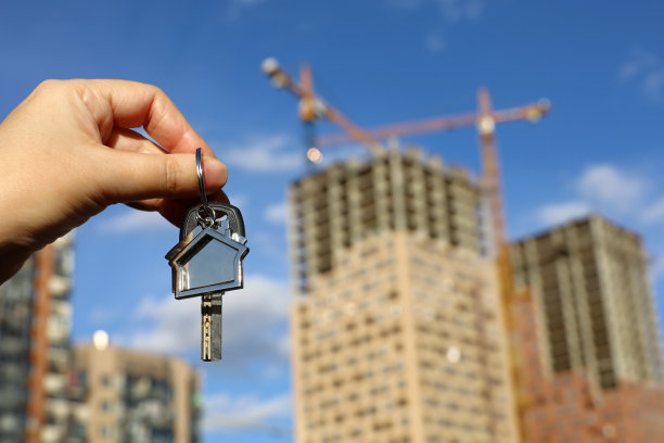 房地产经纪人，房子形状的钥匙链和女性手中的钥匙在建筑起重机和新建筑的背景图片下载