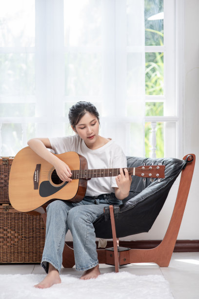 女孩正坐在椅子上弹吉他。图片下载