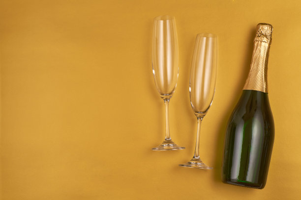 黄色背景上的一瓶香槟和两个空玻璃杯，俯视图。文本的复制空间。图片下载