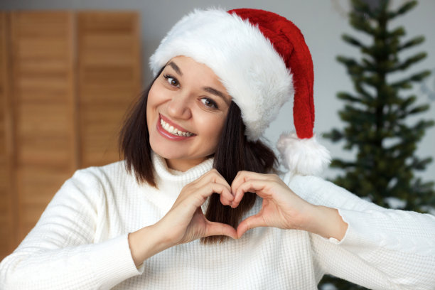 特写肖像可爱的微笑加上尺寸的圣诞老人帽子显示心形的手图片下载