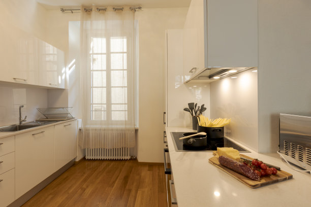 现代白色厨房，镶木地板。炉火上放着盛意大利面的锅，引擎盖上的灯是亮着的。图片下载