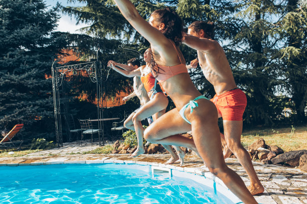 一群年轻的朋友正在跳入游泳池。在炎热的夏天享受乐趣和清爽。图片下载