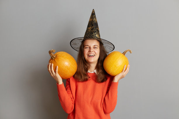 微笑积极的黑发女孩，穿着毛衣，拿着秋天的南瓜，精神抖擞，庆祝十月的万圣节，喜迎丰收，灰色背景下的模特。图片下载