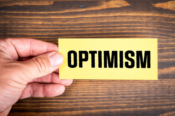 乐观。一张男人手里写着文字的便条纸。木材纹理背景图片下载