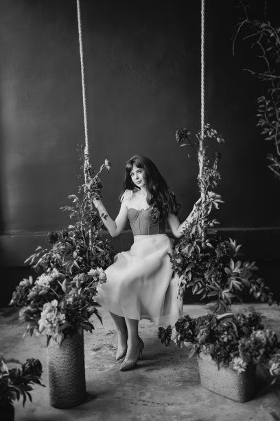 一位身穿白衣的美丽女子坐在牡丹花丛中的秋千上。图片下载