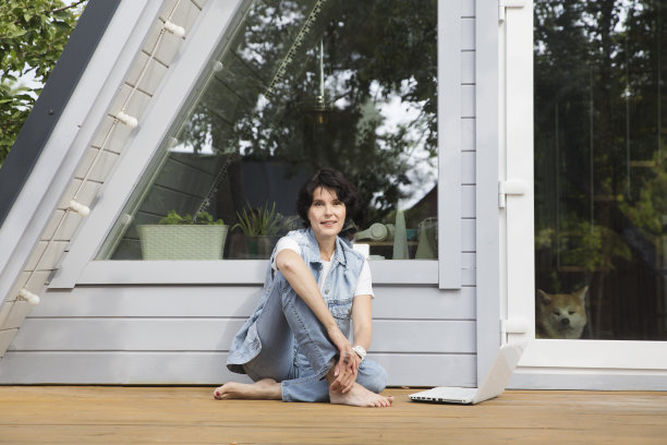 在度假屋工作，远程工作者。一位中年妇女正在房子附近的花园里用笔记本电脑上网。从任何地方工作。图片下载