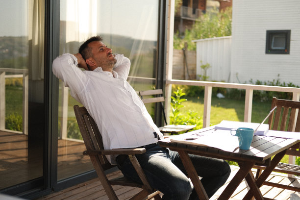 一名穿着便装的男子在田园诗般的乡村花园用笔记本电脑工作。图片下载