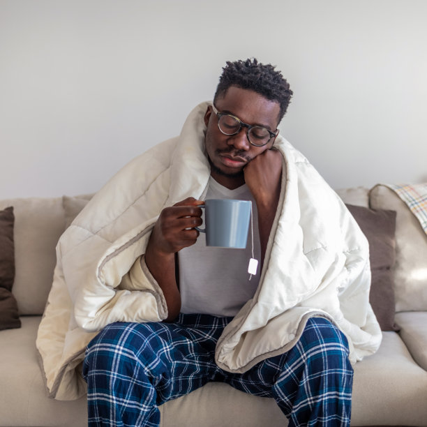 生病的非洲人喝着热茶，头痛欲裂，自由自在。一个患感冒的年轻人在家休养的照片。图片下载