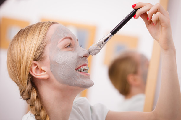 快乐的年轻女子在鼻子上涂泥巴面膜图片下载