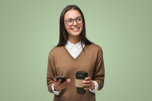 美丽的年轻女子的肖像拿着智能手机和外卖咖啡，隔离在绿色图片下载