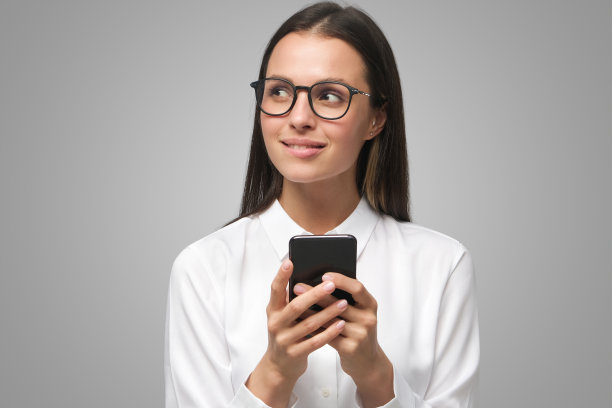 戴眼镜的商务女孩看着左边，在灰色背景的智能手机上输入信息图片下载