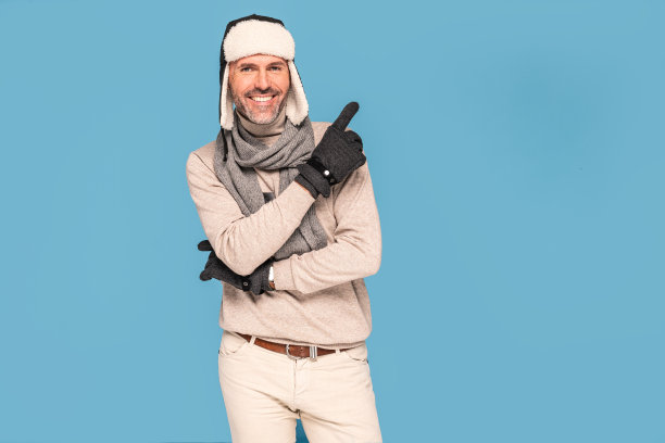 穿着冬装的微笑男子看着相机，指着蓝色粉彩工作室的背景。图片下载