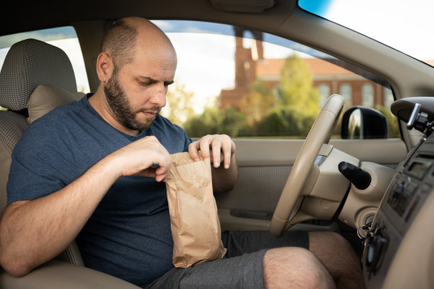 汽车司机在堵车的路上打开一个装着汉堡包的包裹。快餐和外卖图片下载