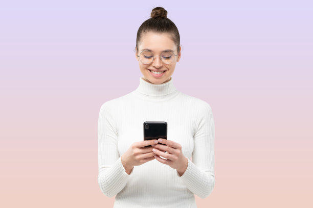 年轻的女学生面带微笑，戴着眼镜，在镜头前用智能手机读短信图片下载