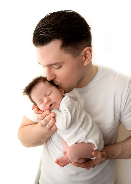 年轻的父亲和新生婴儿的特写画像。父亲将一个美丽的新生女儿抱在怀里，温柔地拥抱、亲吻。爱的概念，幸福的父亲。白色背景的照片。图片下载