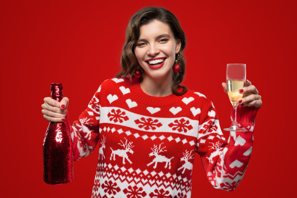 快乐的女人在温暖的圣诞驯鹿毛衣与香槟红背景图片下载