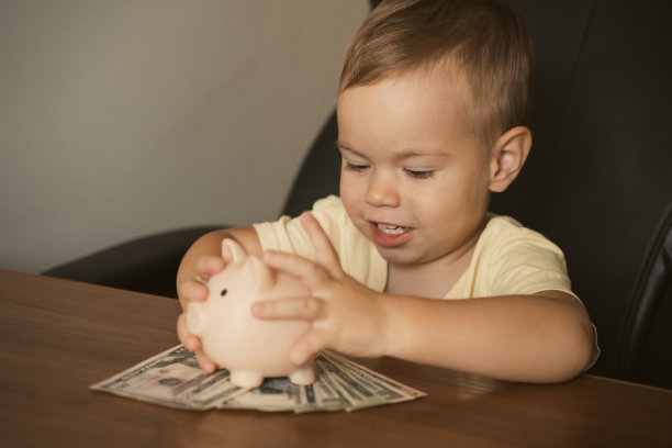 儿童美元钞票储蓄罐在桌子上。聪明快乐的男孩在存钱罐里存钱，学习存钱。金钱、财务、保险和人的概念。图片下载