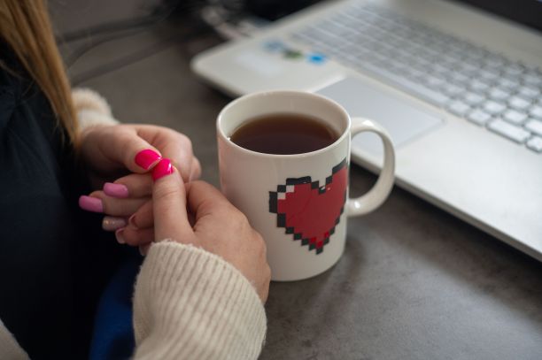 在像素心形马克杯和笔记本电脑附近，特写拍摄了这位女士的手图片下载