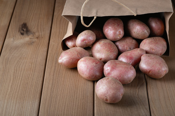 新生的红土豆在纸袋木制背景图片下载