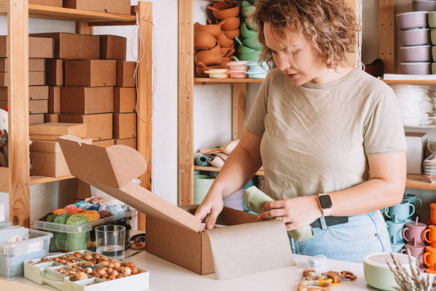 微笑集中卷曲的妇女包装和包装货物与硅胶婴儿盘在盒子里交付。在家里工作图片下载