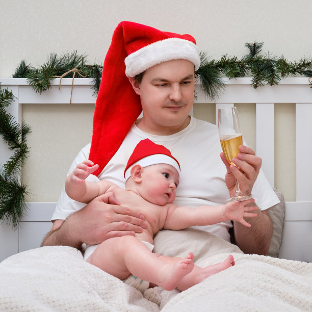 一名男子和一个孩子在一张为圣诞节和新年装饰的床上喝酒图片下载