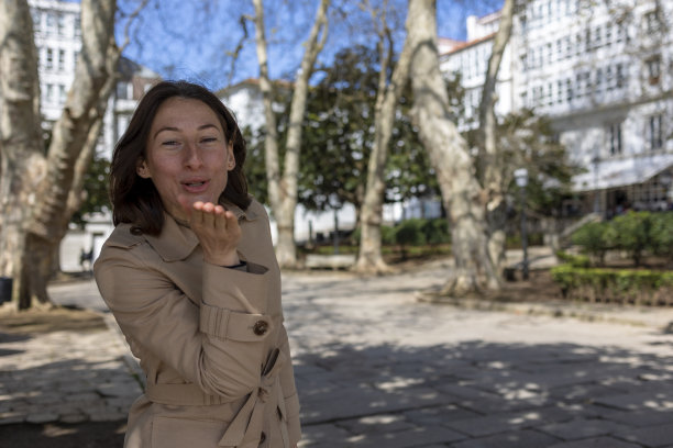 公园里一个穿米色斗篷的女孩送了一个飞吻。图片下载