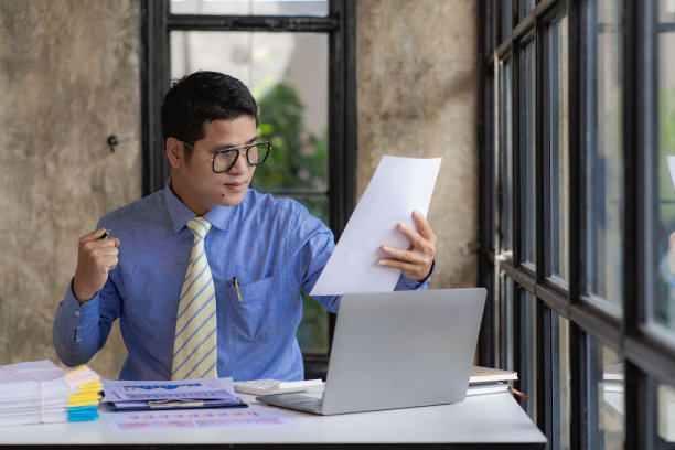 亚洲商人处理成堆的文件，用笔记本电脑分析数据的财务图表，财务办公室的文件，成堆未完成的文书工作，商业年度报告的概念。图片下载