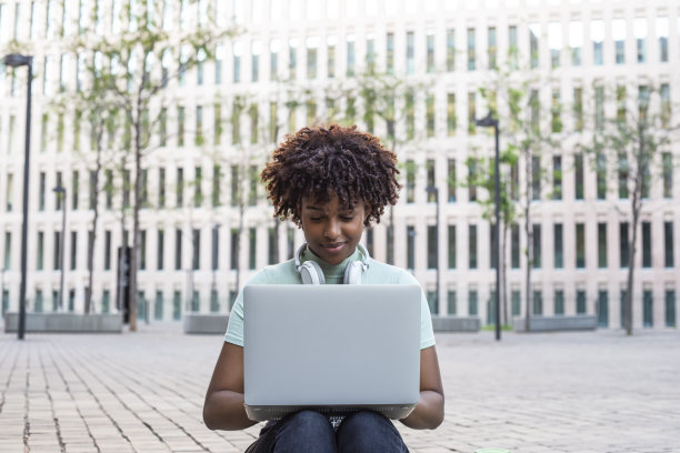 年轻的学生坐在户外的楼梯上，在笔记本电脑上打字图片下载