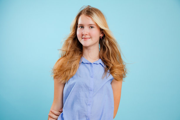 肖像微笑的少女长金发穿着蓝色衬衫，手背后蓝色的背景。图片下载
