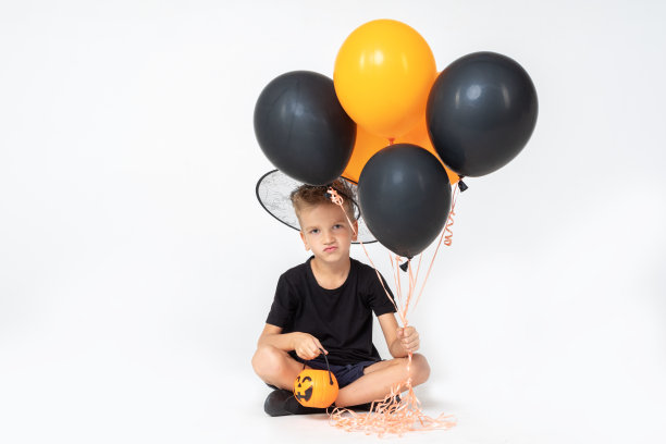 一个快乐的男孩，戴着巫师帽，拿着一个南瓜形状的桶和黑色和橙色的气球图片下载