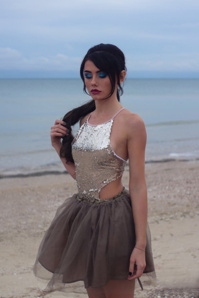 美丽时髦的女孩站在sia的海边，穿着雪纺裙子和闪亮的衬衫在水边图片下载