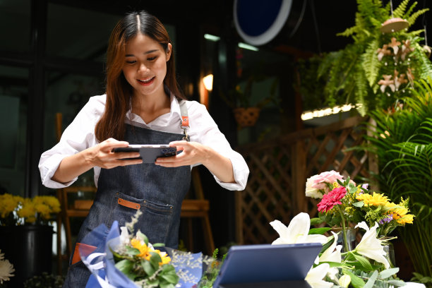 年轻的亚洲女性小企业主使用智能手机为客户订购的鲜花拍下照片。图片下载