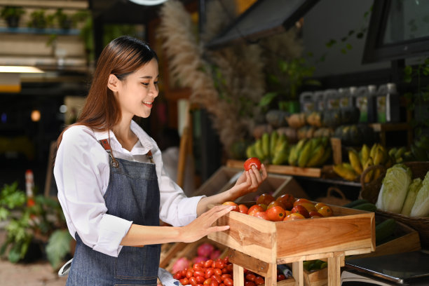 年轻的有机蔬菜摊主在商店货架上摆放西红柿。农贸市场的概念。图片下载