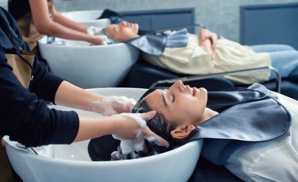 年轻女子在理发店洗完头。一位女士正在为顾客洗头和按摩头发。一名在理发店洗头的女性。图片下载