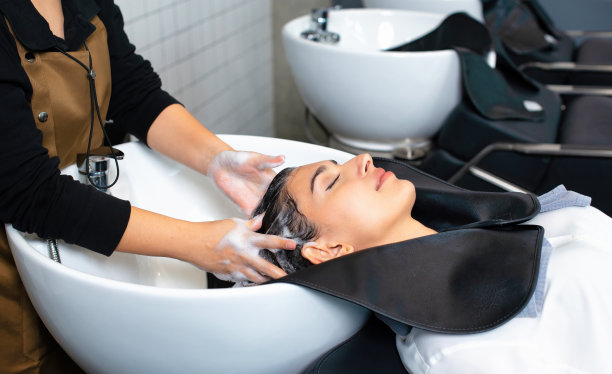 年轻女子在理发店洗完头。一位女士正在为顾客洗头和按摩头发。一名在理发店洗头的女性。图片下载