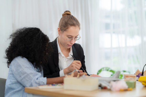 一个年轻的黑人女孩和老师坐在小学的教室里。女老师教她的学生如何用复制空间画画。教育与学术并重，回归学校理念图片下载