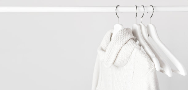 白色的针织羊毛衫挂在白色的木衣架上，背景是浅色的墙壁。秋冬的衣服。店铺概念、销售、设计。文本。图片下载