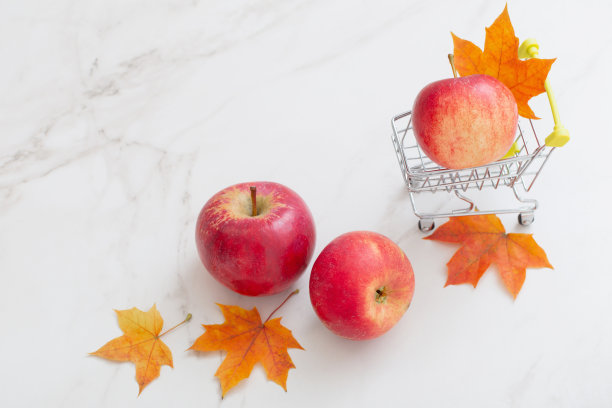 红苹果放在小推车里，枫叶放在白色大理石背景上图片下载