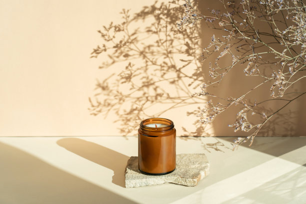 石头上的玻璃杯里装着手工制作的香味蜡烛，米色背景上放着干花。家庭装饰用的木制烛芯蜡烛。潮流色彩背景的自然和休闲的概念。图片下载