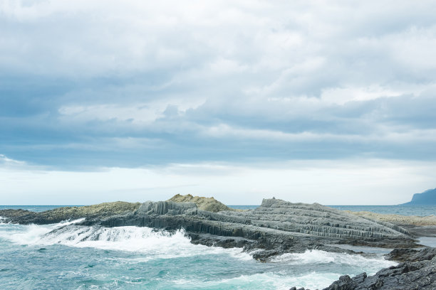 由柱状玄武岩在暴风雨的大海背景下形成的岩石海岸，千岛群岛的海岸景观图片下载