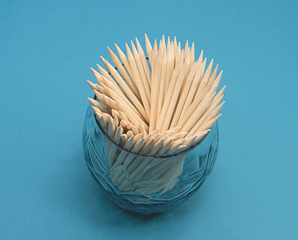 涂指甲用的橙色木棍放在蓝绿色背景的玻璃杯里。图片下载