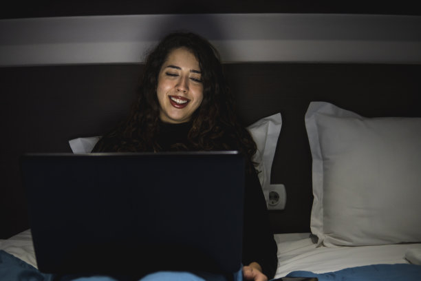 微笑的白人女孩在床上用笔记本电脑图片下载