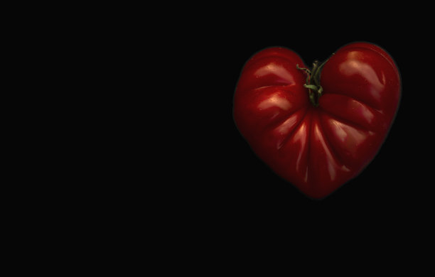 深色背景上的心形番茄。一个牛肉番茄，黑底突出，大的成熟的红色排骨。番茄Cuore di Bue，在对比鲜明的背景上突出图片下载