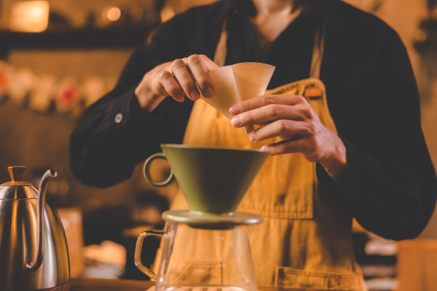 时髦的咖啡师在咖啡馆餐厅的营业店里用热水倒出黑豆冲泡咖啡因饮料，用纸给杯子或马克杯加香，制作滴漏或过滤式的饮料咖啡图片下载